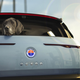 A photo of a black fluffy dog hanging its head out the rear window of a Fisker Ocean SUV.